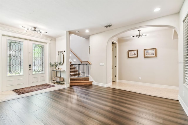 foyer with an inviting chandelier, stairs, visible vents, arched walkways, and wood finished floors