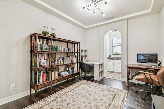 home office featuring a raised ceiling, visible vents, baseboards, arched walkways, and dark wood finished floors
