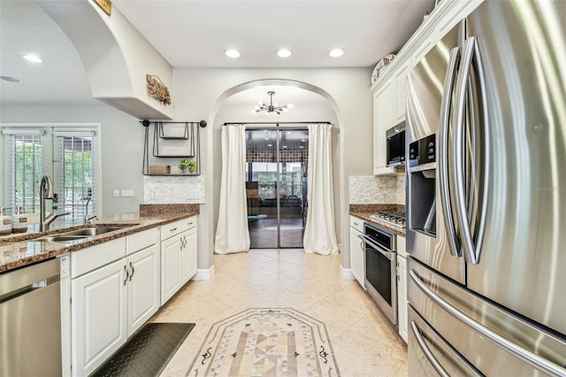 kitchen with dark stone counters, recessed lighting, a sink, stainless steel appliances, and arched walkways