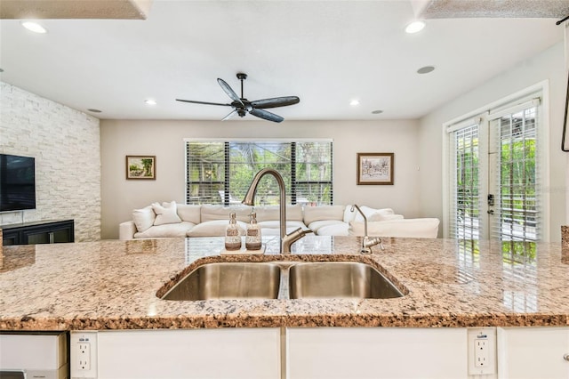 kitchen featuring light stone countertops, a sink, white cabinetry, a ceiling fan, and open floor plan