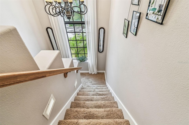 stairway featuring visible vents, a textured wall, baseboards, an inviting chandelier, and carpet