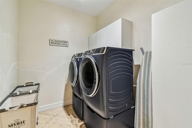 laundry area featuring light tile patterned flooring, baseboards, cabinet space, and washing machine and dryer