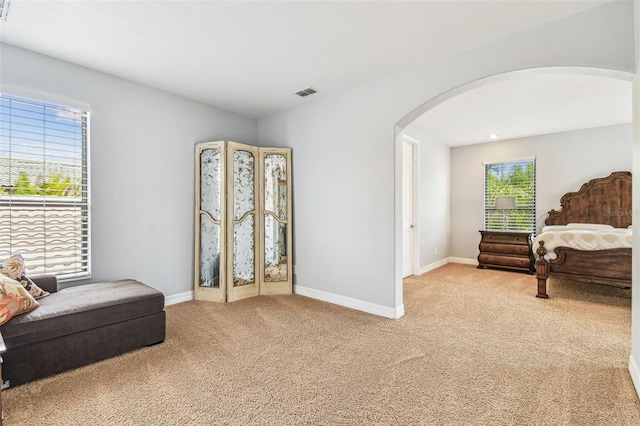 living area featuring arched walkways, visible vents, light colored carpet, and baseboards