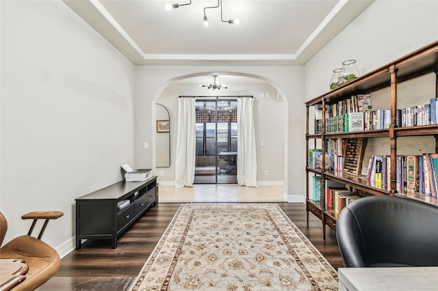 interior space with arched walkways, a raised ceiling, a chandelier, and baseboards
