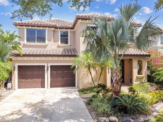 mediterranean / spanish-style house featuring a tile roof, a garage, stucco siding, and decorative driveway