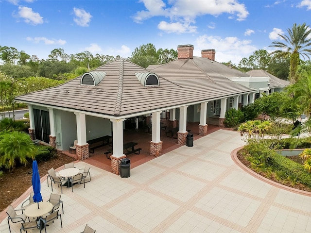 rear view of property with a tile roof, a patio, outdoor dining space, and a chimney