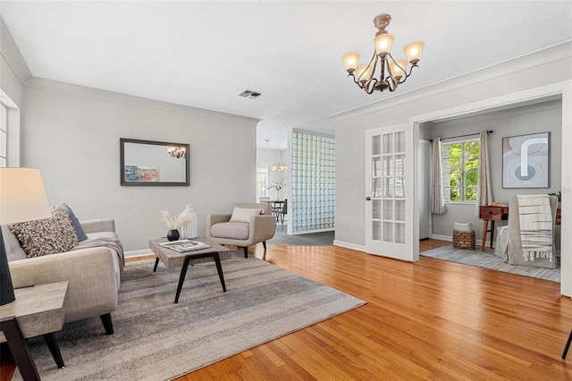 living area with a chandelier, french doors, visible vents, baseboards, and wood finished floors