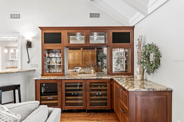 bar featuring wood finished floors, visible vents, indoor wet bar, and vaulted ceiling with beams