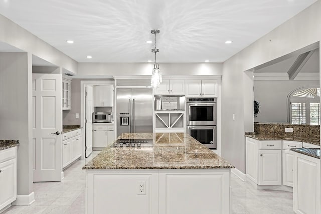 kitchen with white cabinets, appliances with stainless steel finishes, a kitchen island, and dark stone counters