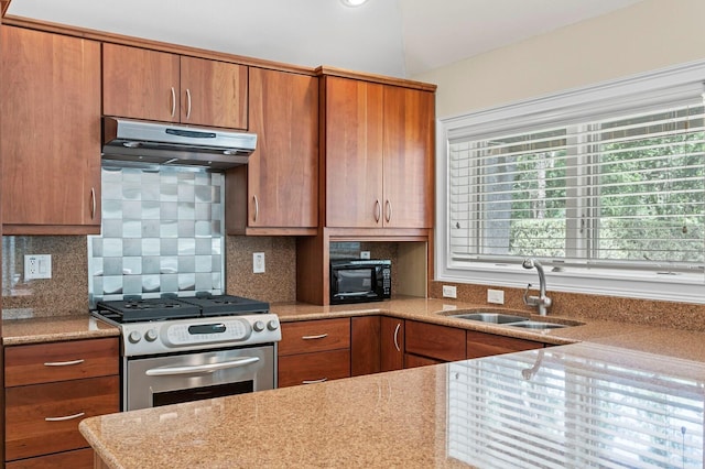 kitchen featuring stainless steel range with gas cooktop, a sink, brown cabinetry, under cabinet range hood, and black microwave