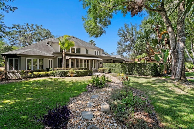 rear view of property with a yard, roof with shingles, and stucco siding