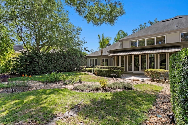 back of property featuring a shingled roof, french doors, and a lawn