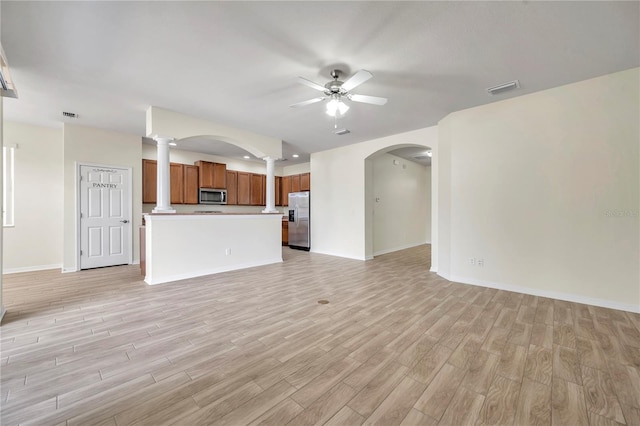 unfurnished living room with ornate columns, a ceiling fan, light wood-style flooring, and baseboards