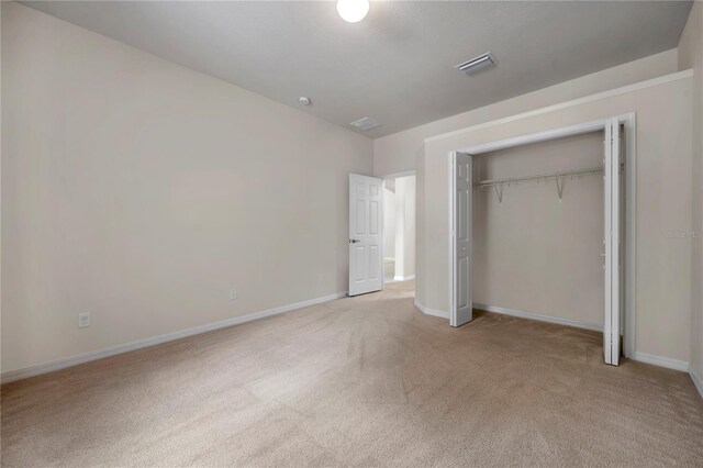 unfurnished bedroom with visible vents, baseboards, a closet, and light carpet