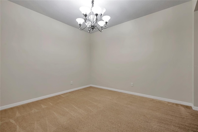 spare room with an inviting chandelier, baseboards, and light colored carpet