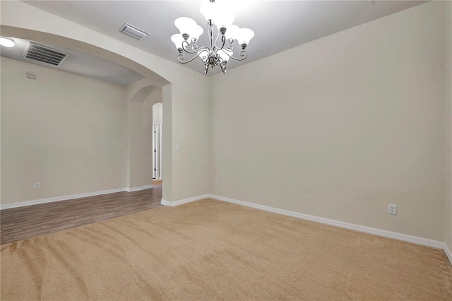 carpeted empty room featuring arched walkways, baseboards, a chandelier, and visible vents