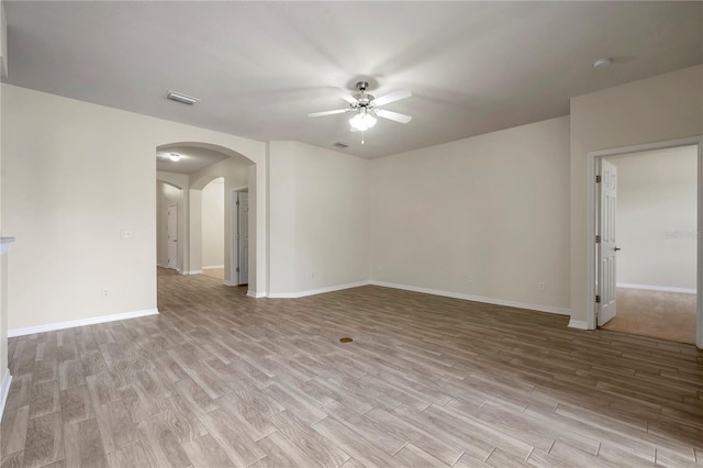 empty room featuring ceiling fan, visible vents, arched walkways, light wood-type flooring, and baseboards