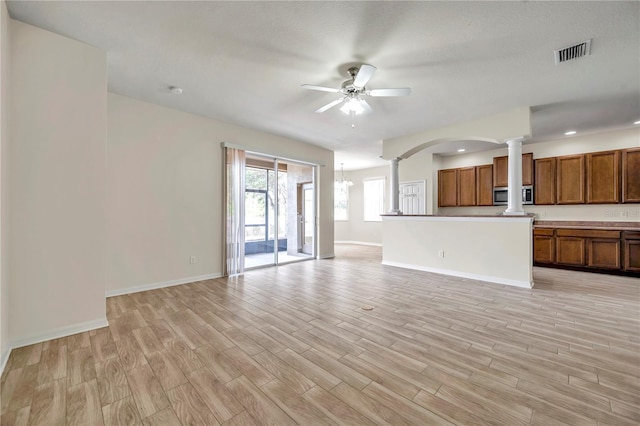 unfurnished living room featuring ceiling fan with notable chandelier, baseboards, light wood-style floors, and decorative columns