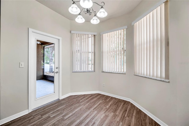 unfurnished room featuring baseboards, wood finished floors, and a chandelier