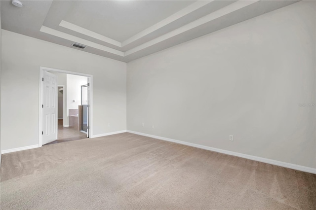 carpeted empty room with a tray ceiling, visible vents, and baseboards