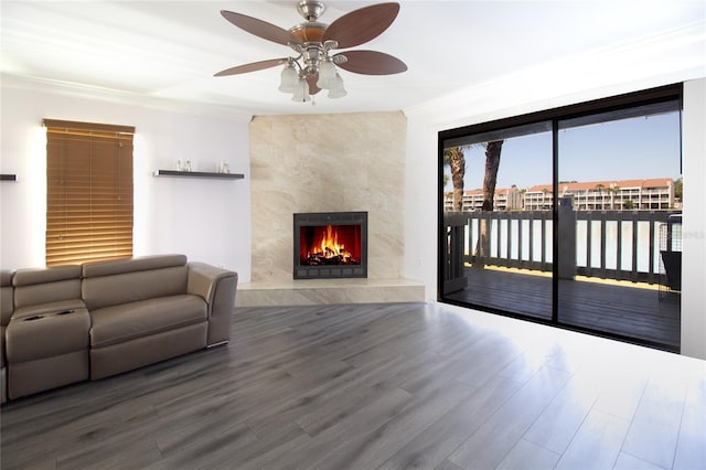 living room with ceiling fan, wood finished floors, a premium fireplace, a water view, and ornamental molding