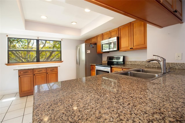 kitchen with appliances with stainless steel finishes, a sink, brown cabinets, a raised ceiling, and a peninsula