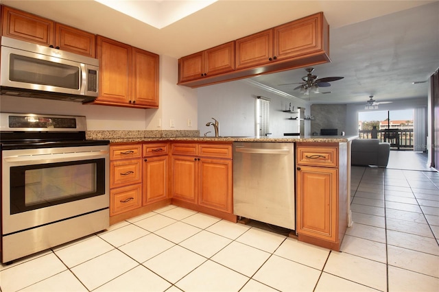 kitchen with appliances with stainless steel finishes, a peninsula, brown cabinetry, and ornamental molding