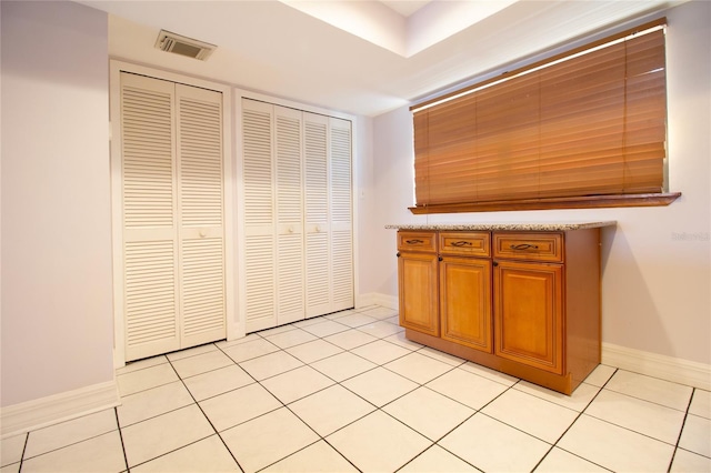 kitchen featuring brown cabinetry, light countertops, light tile patterned flooring, and baseboards