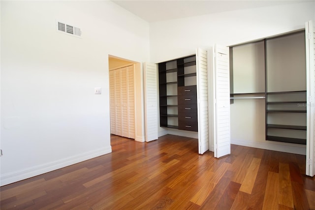 unfurnished bedroom with two closets, baseboards, and wood finished floors