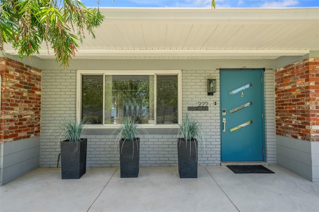doorway to property featuring covered porch and brick siding