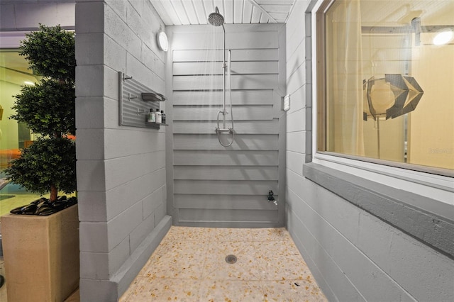 bathroom with a tile shower and concrete block wall