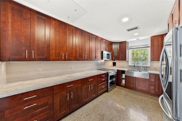 kitchen with a sink, visible vents, stainless steel appliances, light stone countertops, and backsplash