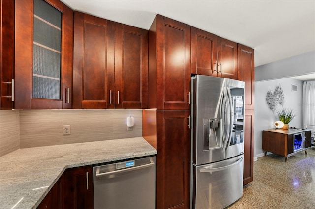 kitchen with light stone counters, decorative backsplash, glass insert cabinets, reddish brown cabinets, and stainless steel appliances