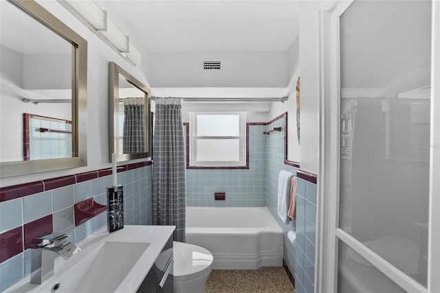 bathroom featuring toilet, a wainscoted wall, tile walls, and visible vents