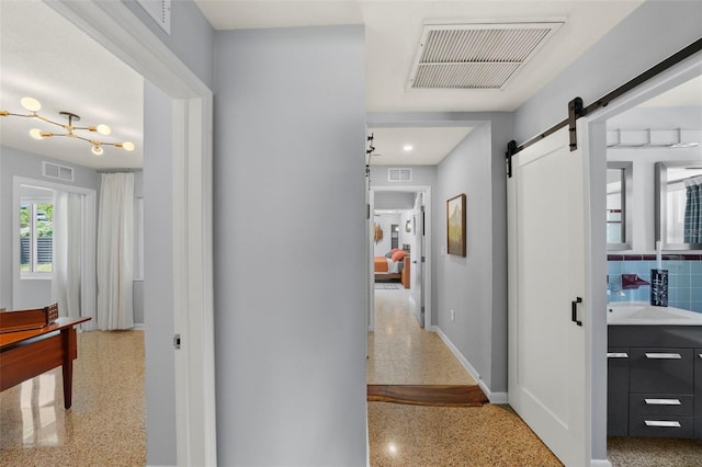 corridor featuring visible vents, speckled floor, and a barn door