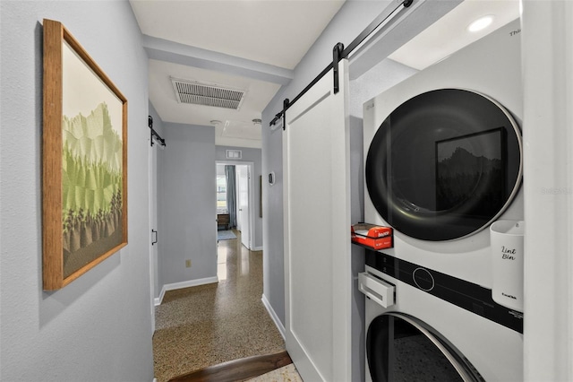 laundry room featuring stacked washing maching and dryer, laundry area, a barn door, baseboards, and visible vents