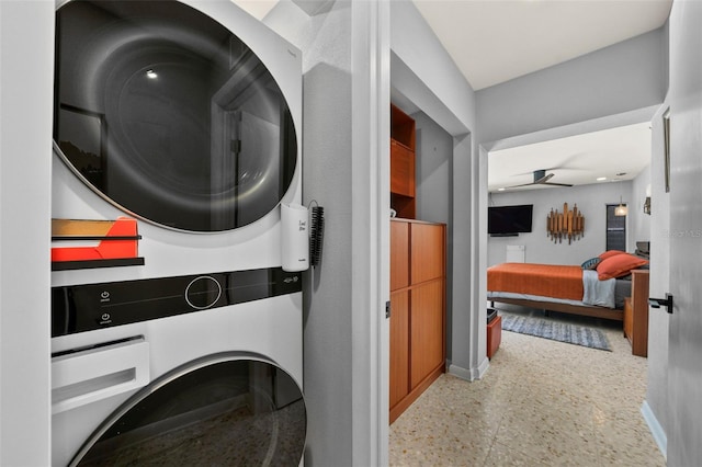 clothes washing area with stacked washing maching and dryer, a ceiling fan, laundry area, and baseboards