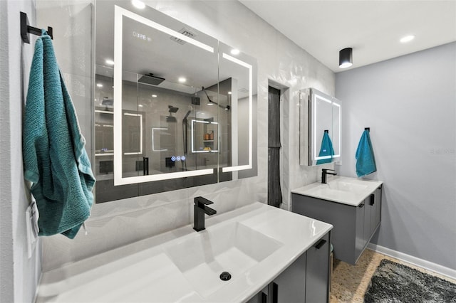 full bath with a stall shower, two vanities, a sink, and baseboards