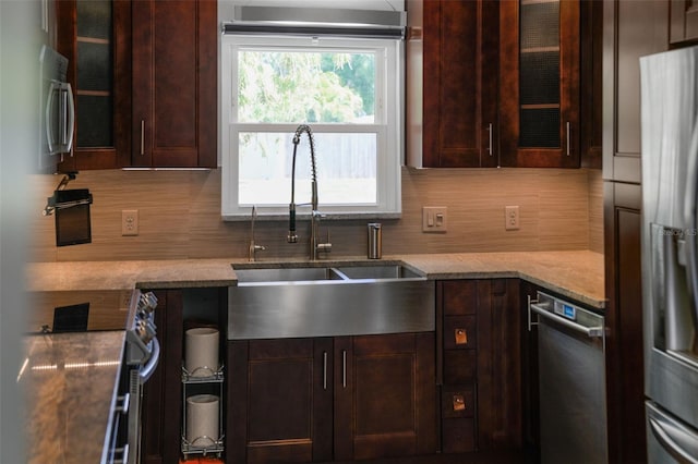 kitchen with light stone countertops, glass insert cabinets, dark brown cabinets, backsplash, and a sink