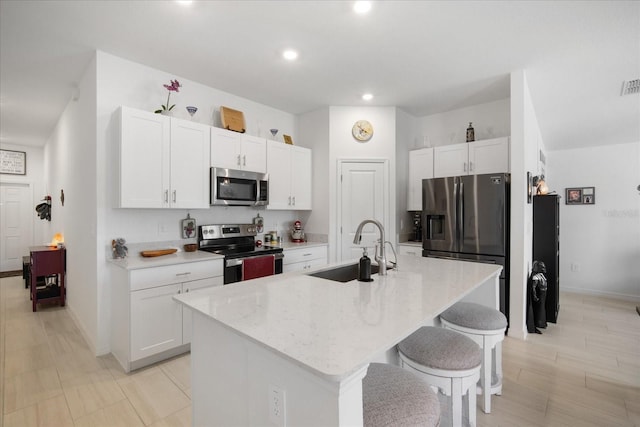 kitchen with a kitchen island with sink, a sink, a kitchen bar, white cabinets, and appliances with stainless steel finishes