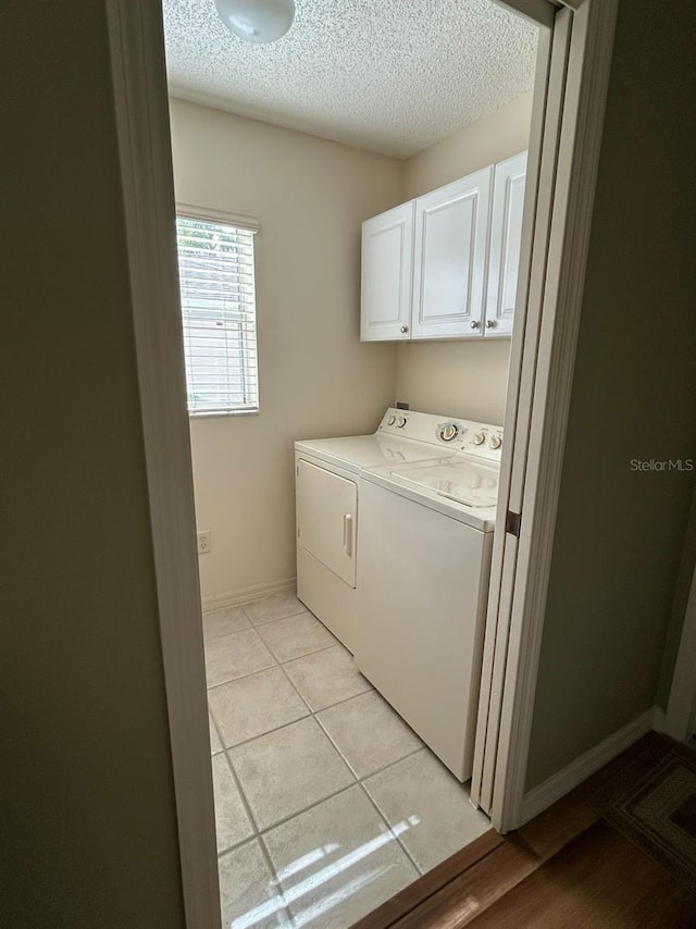 washroom featuring cabinet space, light tile patterned floors, separate washer and dryer, baseboards, and a textured ceiling