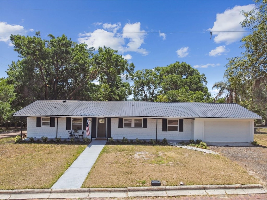 ranch-style house with a garage, covered porch, a front yard, and metal roof