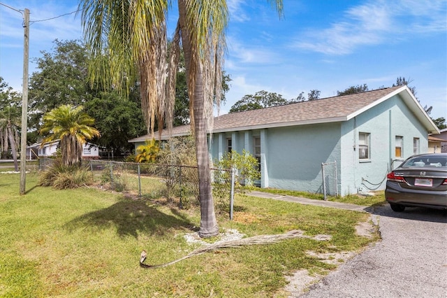 view of property exterior with fence, a lawn, a shingled roof, and stucco siding
