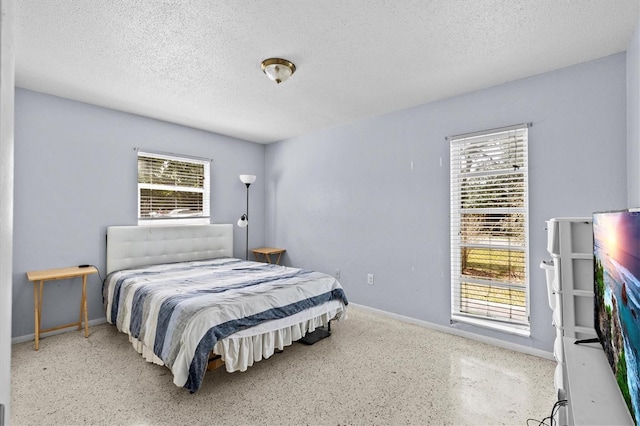 bedroom with speckled floor, baseboards, multiple windows, and a textured ceiling