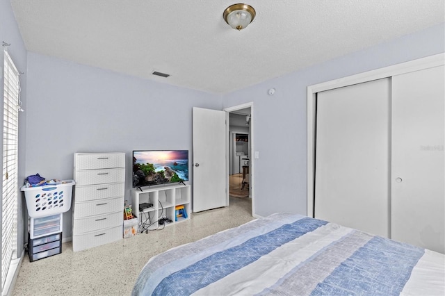 bedroom with speckled floor, visible vents, and a closet