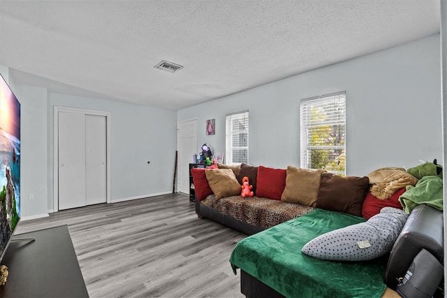 living room featuring a textured ceiling, wood finished floors, visible vents, and baseboards