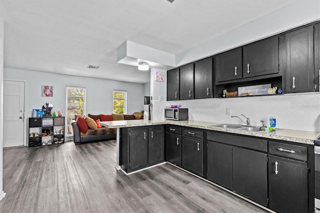 kitchen with open shelves, a sink, open floor plan, light wood-type flooring, and stainless steel microwave