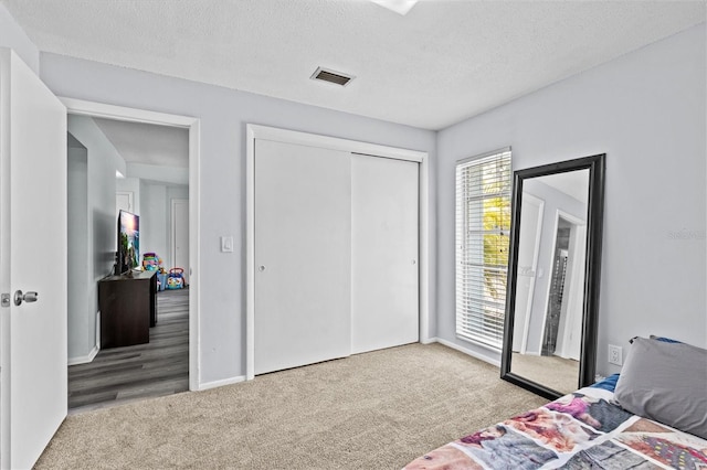 carpeted bedroom with a textured ceiling, baseboards, visible vents, and a closet