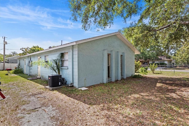 view of side of home featuring stucco siding, central AC unit, and fence
