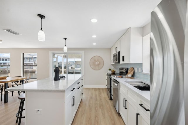 13810 Malcolm Ave, Hudson, FL 34667 - kitchen featuring appliances with stainless steel finishes, light wood-type flooring, a center island, tasteful backsplash, and decorative light fixtures